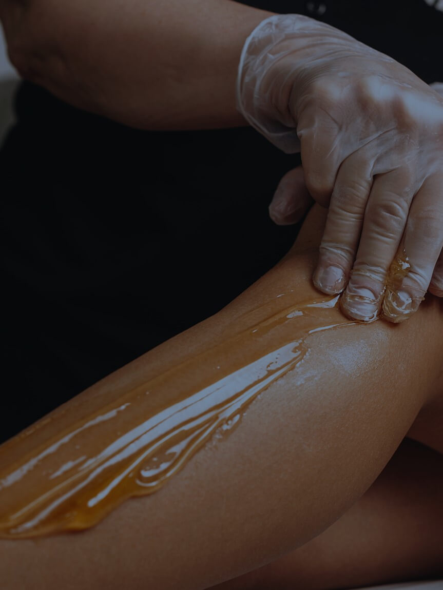 A gloved hand applying a thick layer of botanical hair-removal product to a person's leg.